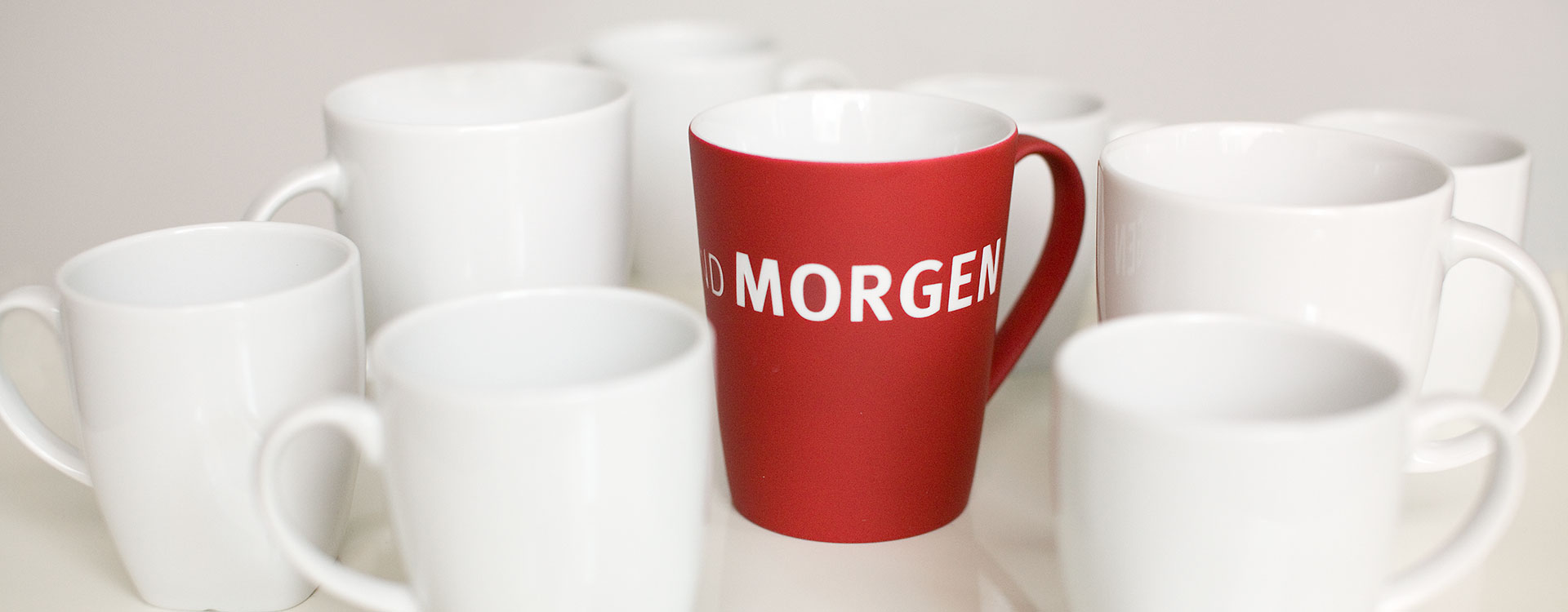 Verschiedene weiße Tassen mit einer roten in der Mitte, auf der HEUTE UND MORGEN steht