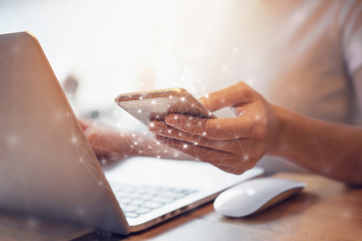 Person mit Handy in der Hand vor einem Laptop